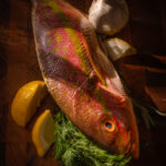 Image shows a colorful yellow tail snapper fish on a cutting board