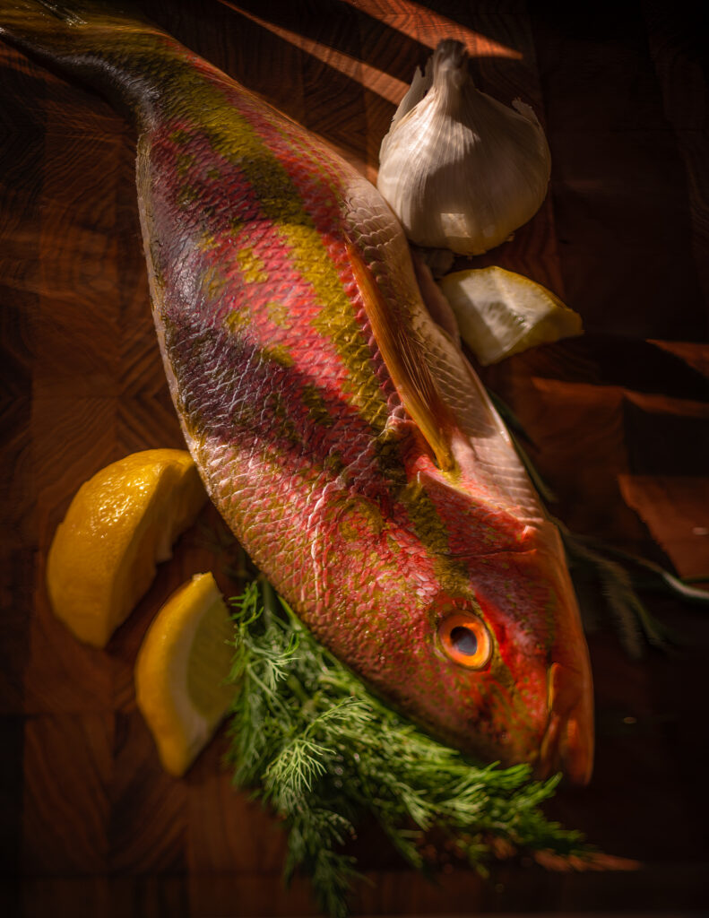 Image shows a colorful yellow tail snapper fish on a cutting board